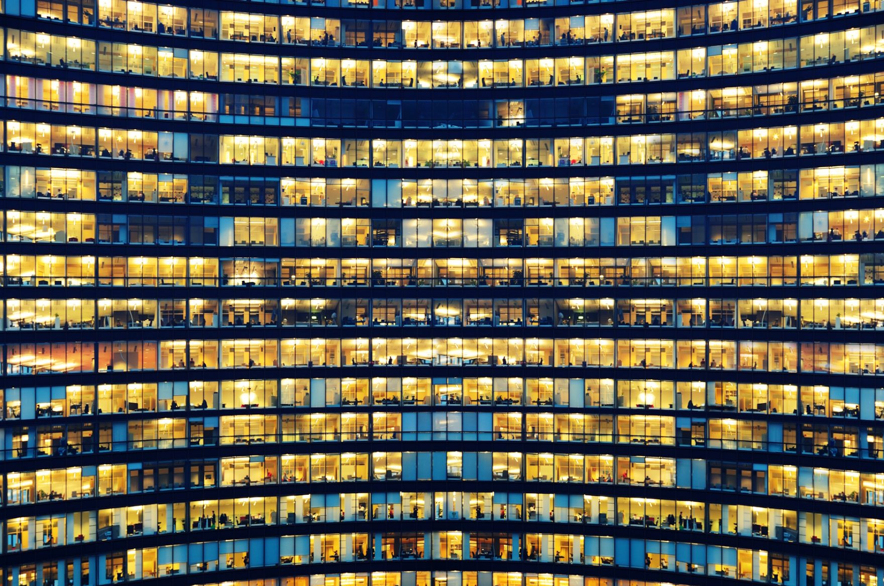 Bürohochhaus bei Nacht mit hell erleuchteten Etagen - Symbol für digitale Zusammenarbeit in Organisationen